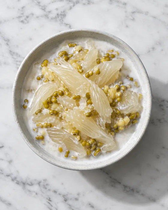 Chè bưởi in a white bowl seen from above: translucent pomelo pith and mung beans in coconut cream